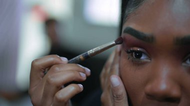 Siyah Latin bir kadının yakın plan yüzü aynanın önünde makyaj yapıyor, 20 'li yaşlarda Afrika kökenli yetişkin bir kız dışarı çıkmaya hazırlanıyor.