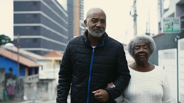Caring African American Adult Son in 50s Walking with Elderly Mother in Urban Street, Authentic Loving Bond with 80s Lady and Family Caretaker in old age