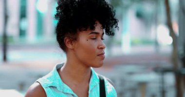 Düşünceli, genç, siyah Brezilyalı bir kadın güneşli bir günde sessizce parka bakıyor.
