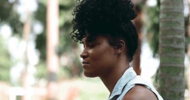 一人の熟考の若い黒人女性プロフィールは厳粛な瞑想感情を持つ公園の外に座っている深い精神的な反射で閉じた顔 — ストック動画