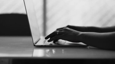 Laptop bilgisayarında daktilo eden yakın çekim elleri, modern teknolojiyi kullanan 20 'li yaşlardaki genç birinin monokromatik siyah beyaz klipsi.