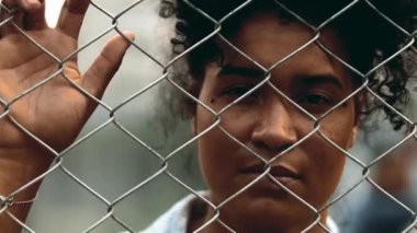 Metal çit bariyerinin arkasında, kriz sırasında yalnızlığı ve umutsuzluğu gösteren ciddi bir siyah kadın var. 20 'li yaşlarda ayrılık ve zihinsel umutsuzlukla boğuşan biri.