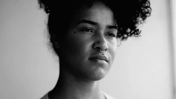 一个有思想的年轻黑人妇女从公寓的平衡窗口看问题 严肃表达的特写镜头 20多岁的非洲裔美国人 有着沉思的单色心情 — 图库视频影像