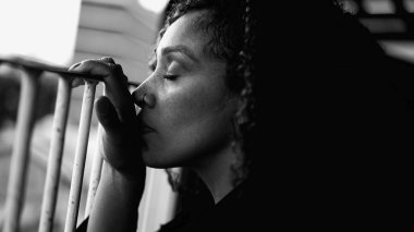 Üzgün, kederli, siyah bir kadın depresyondan gözleri kapanıyor balkondan metal çubuğa yaslanarak evde dramatik siyah beyaz monokromla sessiz bir umutsuzlukla mücadele ediyor.