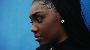 Düşünceli bir siyah ergen kız, düşünceli bir yüz ifadesiyle, yakın plan yüz takibi görüntüsü derin ruhsal yansıması olan şehir sokaklarını seyrediyor.