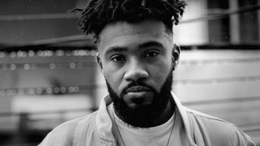 Ciddi bir Güney Amerikalı genç adamın portresi. Çiselemeli yağmurun altında 20 'li yaşlarda, koyu siyah beyaz bir yüz ifadesiyle kameraya doğru dönüyor.