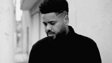 İçsel bir genç siyahi, derin duygulara sahip, sokakta durmuş, ciddi bir şekilde yere bakıyor, bir ikilemi düşünüyor, siyah ve beyaz bir kararla ilgili kafa yoruyor.