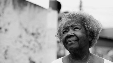 Düşünceli, yaşlı bir Afrikalı Amerikalı kadın şehir sokağında dikilip tek renkli, siyah beyaz gökyüzüne bakıyor. 80 'lerdeki Sadık Yaşlı Kadın
