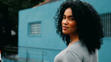 Güçlü genç siyahi bir kadın, Güney Amerika 'daki şehir caddesinde ilerlerken başını kameraya çeviriyor. Kıvırcık saçlı, gururlu, Afrika kökenli, kendine güvenen ve neşe saçan biri.