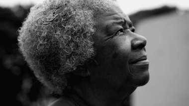 80 'li yaşlarda düşünceli bir Afrikalı Amerikalı kadın gökyüzüne doğru derin bir meditasyonla bakıyor. Yoğun monokromatik, siyah ve beyaz olarak dışarıda duruyor.