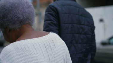 Afrika kökenli Amerikalı son sınıf öğrencisi, orta yaşlı oğlunun yardımıyla sokaklarda geziniyor. Şehir ortamında çekim yaparken ileri doğru yürüyor.