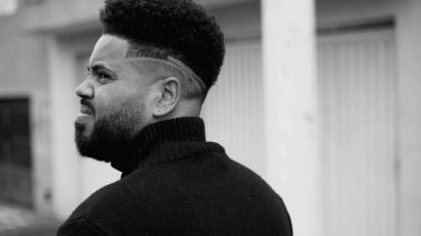 Ciddi bir ifadeyle şehir caddesinde yürüyen dalgın genç bir zenci. Dalgın Güney Amerikalı adam şehir ortamında siyah beyaz geziniyor, yakın plan çekimleri takip ediyor.