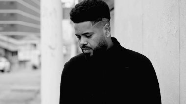 İçsel bir genç siyahi, derin duygulara sahip, sokakta durmuş, ciddi bir şekilde yere bakıyor, bir ikilemi düşünüyor, siyah ve beyaz bir kararla ilgili kafa yoruyor.