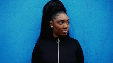 Düşünceli, genç, siyah bir kadın, düşünceli bakışlarla sokağı gözetleyen mavi duvara yaslanıyor. 20 'li yaşlarda Afro-Amerikalı bir kız portresi