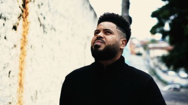 Düşünceli ve düşünceli bir ifadeyle dışarıda yürüyen ve derin düşüncelere dalmış kentsel çevreye bakan içsel bir siyahi.