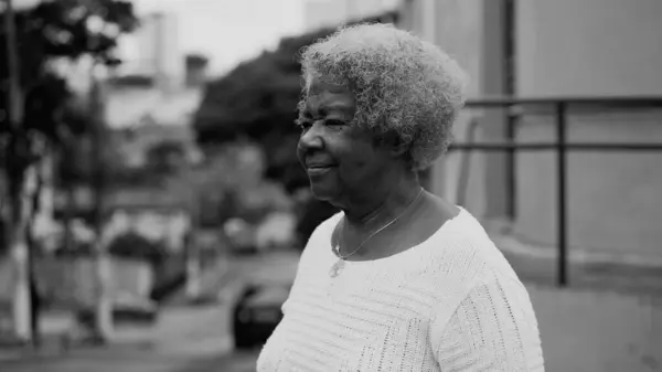 One older black woman in 80s walking in urban setting, tracking shot body of African American elderly lady with gray hair strolling in street, black and white