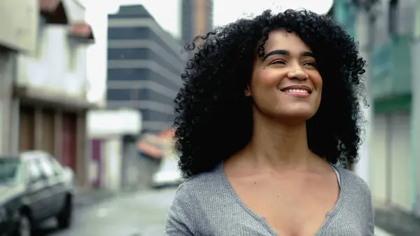 One empowered African American young woman walks forward in street, tracking shot close-up face of confident curly haired adult girl in 20s exuding joy and happiness