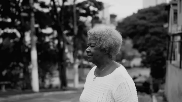 One older black woman in 80s walking in urban setting, tracking shot body of African American elderly lady with gray hair strolling in street, black and white