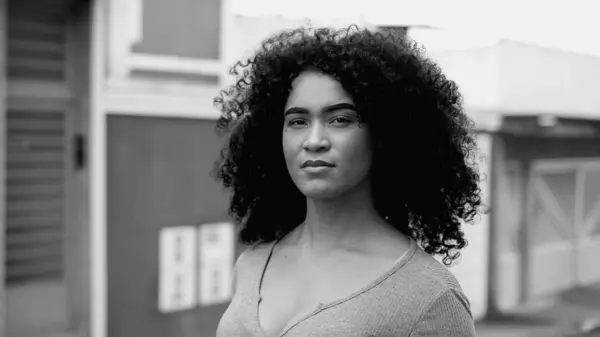 Empowered African American Woman in Urban Setting, Tracking Close-Up of Confident Young Female Face in bold black and white, monochromatic. One black person standing in street staring at camera