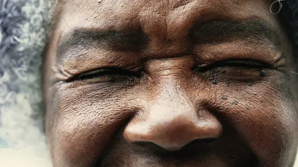 One peaceful wrinkled South American black woman closing eyes in meditation in macro closeup, opening eye staring at camera, detail face of elderly person in 80s