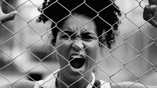 一位怒气冲冲的年轻黑人妇女靠在金属栅栏上对着摄像机尖叫 感到绝望 20多岁的非洲裔美国人在黑白色的障碍物后面绝望地挣扎着 — 图库视频影像
