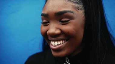 Mavi duvarda gülümseyen genç bir İspanyol kadın, 20 'li yaşlarda Afrika kökenli mutlu bir yüz ifadesiyle yakın plan bir kız.