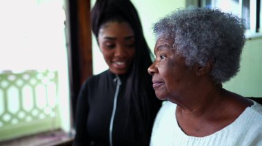 Afrika kökenli Amerikalı torun, yaşlı büyükannesine bakıyor. Kolları omzunda, 80 'lerde yaşlı bir kadına yardım ve destek gösteriyor. Nesiller arası aile içi bakım.