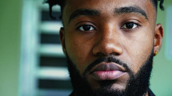 Портрет чернокожего молодого человека, смотрящего в камеру с торжественным серьезным выражением лица, крупным планом лица человека африканского происхождения в возрасте 20 лет