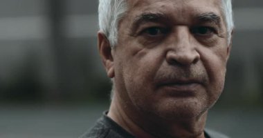 Buruşuk, ciddi, sert yaşlı bir adamın portresi. Şehir merkezinde durmuş, ciddi bir ifadeyle kameraya bakıyor. 70 'li yaşlıların yakın çekim görüntüsü.