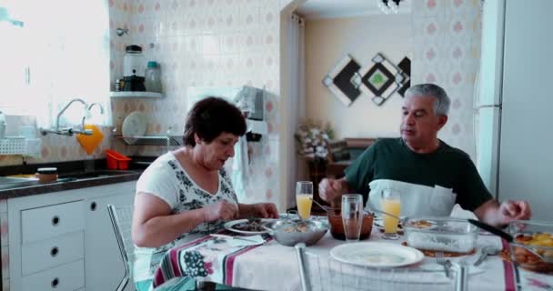 居心地の良いホームキッチンで高齢のペアダイニング 本物のシニアスパウスは 食事を共有しています 結婚したカップルは昼食を食べ 引退年齢を描いた妻に仕える夫 — ストック動画