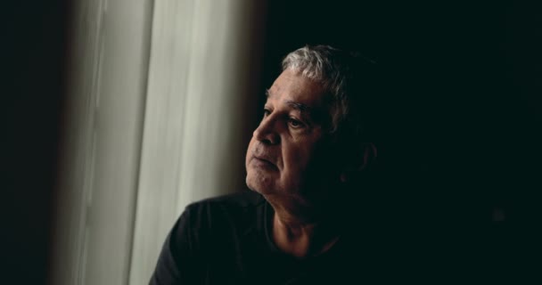 坐在窗边沉思的老人沉思地凝视着外面 坐在描绘退休年龄的闷闷不乐的房间里的可怜巴巴的 真实的 沉思的老年人 — 图库视频影像