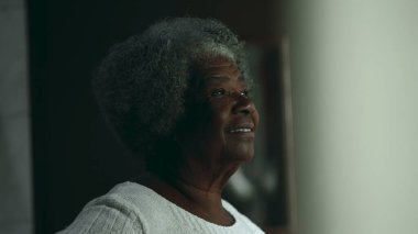 80 'li yaşlarda, mesken penceresinden bakan mutlu, düşünceli, yaşlı bir zenci kadın. İçten, düşünceli, kıdemli, Afrikalı Amerikalı kadın.