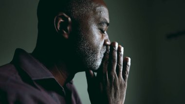 Derin düşüncelere dalmış bir siyahi kıdemli adam zor zamanlarda umudu ve inancı olan, loş bir odada, gözleri kapalı dua ediyor. Ruhani Afrikalı Amerikalı 50 'li yaşlarda