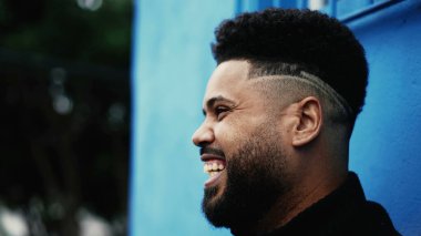 Mutlu bir Latin asıllı genç adam kamerasız biriyle konuşurken gülüyor ve gülümsüyor.