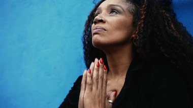 Endişeli bir Latin kadın zor zamanlarda teselli arıyor. Umutla ve inançla yukarılara bakan şehirde Tanrı 'ya dua ediyor.