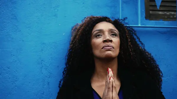 One worried hispanic black woman seeking solace during hard times Praying to GOD in urban setting gazing upwards with HOPE and FAITH