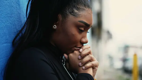 Stock image One pensive young black woman pondering decision with hands clenched together standing outside with thoughtful gaze struggling with dilemma in in urban setting