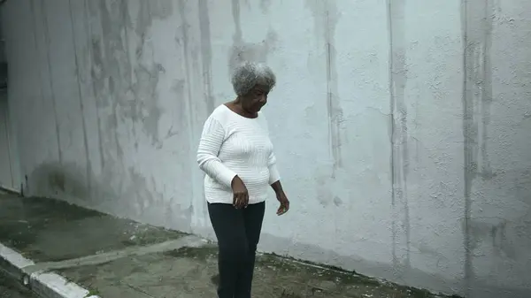 Elderly South American black woman arrives home from sidewalk street, opens residence front door returning by closing gate behind her, senior 80s person of African descent