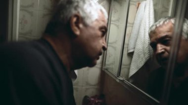 Bunalımlı kıdemli bir adam kendi yansımasına bakıyor zihinsel hastalıkla boğuşuyor inançsızlıkla başını sallıyor. Stresli, 70 'li yaşlarda, beyaz saçlı ve buruşuk suratlı beyaz bir adam.