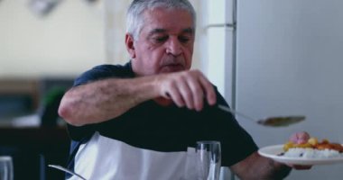 70 'li yaşlarda, kır saçlı, evde yemek servisi yapan, emeklilik yıllarında samimi bir an yaşayan bir adam.