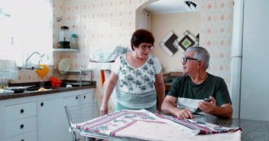 Üst düzey koca yaşlı eşine cep telefonu ekranı gösteriyor. Mutlu adam sosyal medyayı ilginç mutfak konutlarında kadın ortağa paylaşıyor.