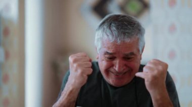 Kendinden geçmiş kıdemli adam cep telefonu cihazıyla ilgili olumlu haberleri kutluyor. Yaşlı insanın kollarını kaldırması ve beklenmedik başarısının gerçek mutlu ifadesi.