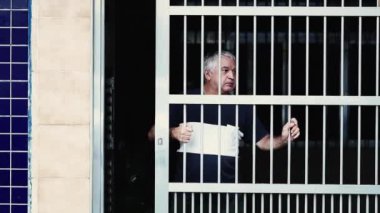 Kıdemli adam evinin kapısından yana kayıyor ve çevreyi gözetliyor. Dışarıda neler olup bittiğini merakla izleyen yaşlı bir adam.