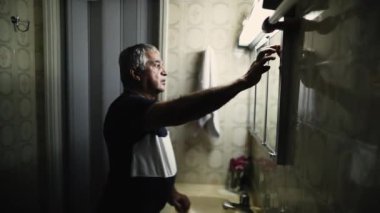 Son sınıf öğrencisi aynanın önünde durarak banyonun floresan ışığını açıyor.