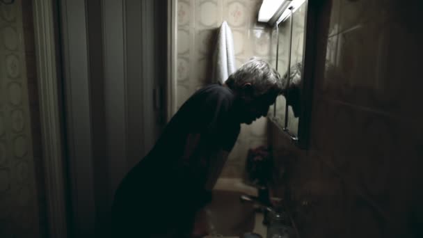トイレの鏡に傾いている抑圧された上級男性は 問題に圧倒され 古い年齢のストレスと占拠に悩まされ 謙虚な住宅で劇的なシーン — ストック動画
