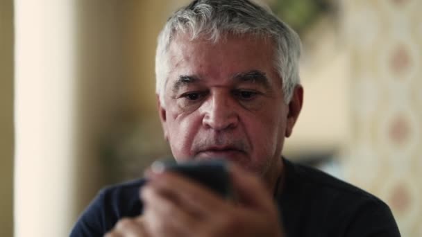 Ζαρωμένος Ηλικιωμένος Άντρας Κοιτάζει Μια Συσκευή Κινητού Τηλεφώνου Μια Ουδέτερη — Αρχείο Βίντεο