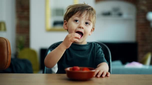 可爱的2岁小男孩在自家厨房柜台边吃草莓 背景可以俯瞰客厅 金发碧眼的高加索小孩偷拍的肖像 — 图库视频影像