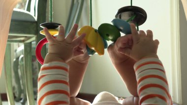 Ayaklarını elinde tutan ve tahta oyuncaklarla oynayan sevimli bir bebek.