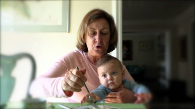 Büyük anne kahvaltı yapıyor kucağında bebek torunu var.