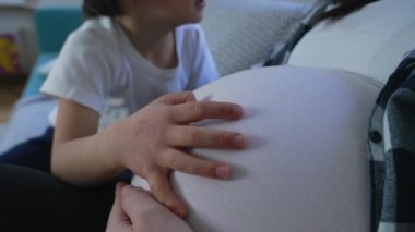 Hamileliğin üçüncü üç ayında annenin karnının üzerinde dinlenen bir çocuğun eli, erkek kardeş ve doğmamış bebek arasındaki annelik kavramı, nazik bir dokunuş.